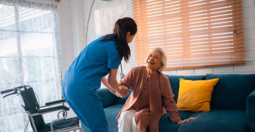 Senior woman smiling getting helped off the couch by a caregiver in assisted living facility