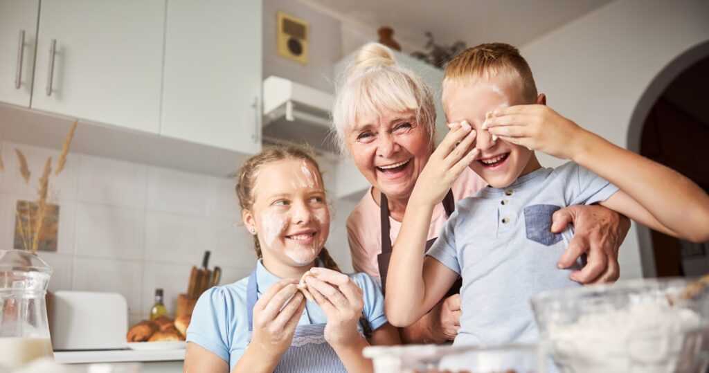 Joyous senior woman and her grandchildren laughing and playing with cookie dough