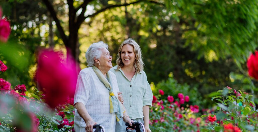Granddaughter walks with senior grandmother with a walker through a garden